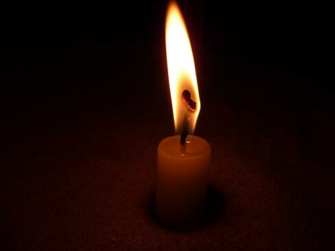 Einzelne brennende Kerze im Dunkeln